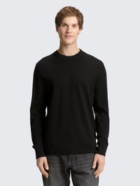 Pull en maille noire avec un col rond, des manches longues et des poignets et ourlet côtelés. Porté avec un jean foncé, design minimaliste.