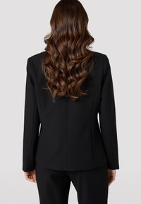 Černý přizpůsobený blazer s fitted střihem, hladkým povrchem a dlouhými rukávy. Minimalistický design bez viditelných kovových prvků či akcentů.