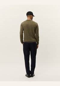Donkerblauwe trousers gecombineerd met een olijfgroene blouse met lange mouwen, met een eenvoudige textuur. Een marineblauwe pet maakt de outfit compleet.