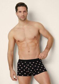 Černé boxerky se vzorem růžových kreslených tváří, s měkkým pasem a přiléhavým střihem, které nosí mužský model.