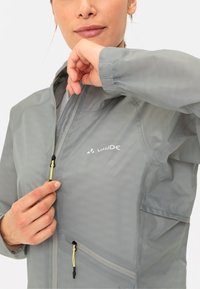 Giacca leggera grigia impermeabile con texture in rete, zip frontale, polsini regolabili e doppie tasche con zip. Logo sul petto sinistro.