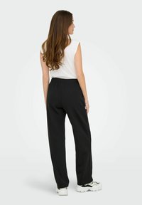 Zwarte wijd-uitlopende sweatpants met een elastische tailleband, gecombineerd met een witte mouwloze top, weergegeven vanuit de achterkant, met een gladde textuur.