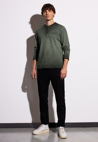 Zelená dlouhý rukáv henley košile s knoflíkovým límcem, nošena s černými kalhotami a bílými teniskami. Hladká textura, žádné výrazné vzory ani akcenty.