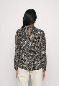 Blusa de manga longa preta e bege com um padrão de estampado de leopardo, detalhe na parte de trás em forma de olho e punhos franzidos. Tecido suave, corte relaxado.