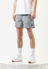 Grå svømmetights med struktureret stof, elastisk talje og snørelukning. Sort mærke detalje på venstre side; model bærer hvide sneakers.