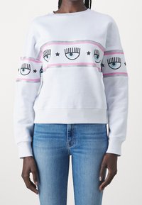 Vit sweatshirt med grafiska tryck av ögon och stjärnor, accentuerad med rosa och silverfärgade ränder. Tillverkad av mjukt material, med ribbade ärmslut.