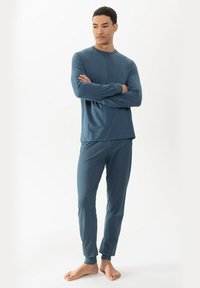 Langsleeve, ronde hals top en taps toelopende broek in donkerblauw, voorzien van een gestructureerde stof en een wit stippenpatroon op de broek.