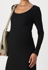 Schwarzes geripptes Langarmkleid mit einem Rundhalsausschnitt, kombiniert mit einer grünen Schultertasche. Der Stoff wirkt weich und hat eine figurbetonte Silhouette.