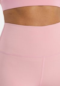 Top atletico rosa chiaro con una texture liscia e elastica e un design con tagli. Presenta un cinturino alto e cuciture piatte per il massimo comfort.