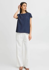 Top navy blu con maniche corte e vestibilità morbida, tessuto testurizzato, scollatura rotonda, abbinato a pantaloni bianchi a gamba larga e sandali con tacco marroni.