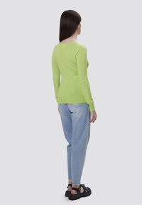 Maglietta a maniche lunghe, leggera, verde lime con un design aderente, abbinata a jeans blu a vestibilità rilassata e sandali neri spessi.