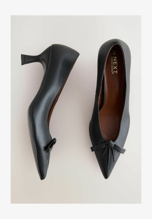 Črne ženske čevlje z visokimi petami, narejeni iz gladke usnjene površine, z ostrim nosom in poudarkom v obliki pentlje spredaj. Stracten, eleganten dizajn.