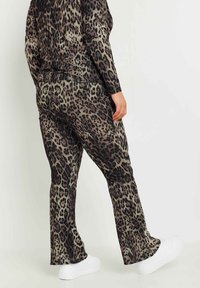 Kattmönstrad loungewear-set i nyanser av brunt och svart, bestående av en långärmad topp och utsvängda byxor, som kombineras med vita sneakers.