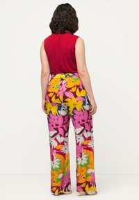Top rosso senza maniche abbinato a pantaloni a fantasia floreale colorata con fiori rosa, gialli e arancioni su sfondo bianco.