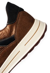 Baskets en daim marron avec des accents métalliques bronze, un panneau texturé noir et une semelle en caoutchouc blanche présentant un motif hexagonal.