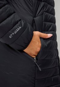 Sort isoleret jakke med quiltet design, lynlåslomme og broderet logo på ærmet. Glat, blank tekstur.