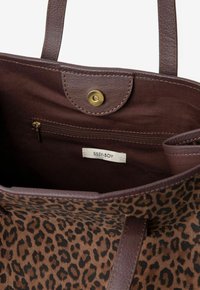 Sac fourre-tout à imprimé léopard avec des accents en cuir marron, une fermeture magnétique et une poche zippée intérieure. L'étiquette indique "SISSY-BOY."