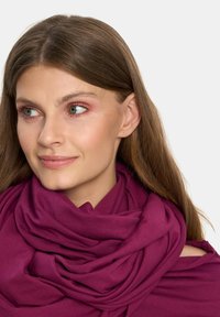 Teksturowany, głęboki magenta szalik owinięty wokół szyi, charakteryzujący się miękkim, płynącym wzorem z warstwowymi fałdami.