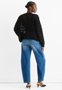 Black knitted sweater with a loose fit and open weave, paired with loose blue denim jeans. Black slingback heels complete the look.