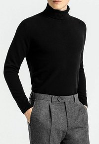 Schwarzer Rollkragenpullover mit geripptem Kragen und taillierter Passform, kombiniert mit grauen, taillierten Hosen mit Falten und Knopfverschluss. Weiche Textur.