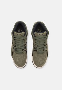 Olivgröna sneakers med en texturerad mockaovandel, perforeringar för andningsförmåga och svarta accenter. Har platta snören och en gummisula.