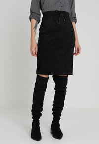 Svart mockapennkjol med dragsko i midjan. Styler med knähöga svarta mockastövlar för en koordinerad look.