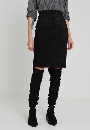 Jupe crayon en daim noir avec taille à cordon. Assortie à des bottes noires en daim jusqu'aux genoux pour un look coordonné.