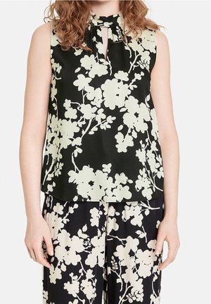 Blouse sans manches en tissu noir avec un motif floral en vert pâle. Détail en forme de goutte au niveau du cou et coupe décontractée.