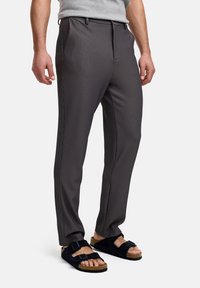 Pantalones a rayas grises hechos de una tela suave con un corte entallado, combinados con sandalias de ante negro con correas ajustables.