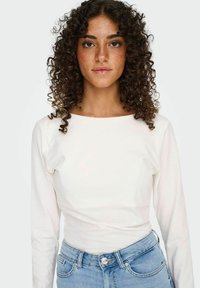 Langærmet hvid bluse med rund halsudskæring, parret med lyseblå denimjeans. Glat stof, tætsiddende design med subtil struktur.
