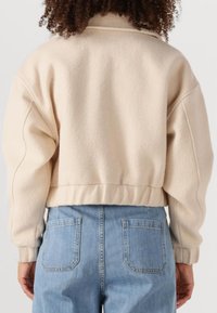 Beige, korte fleece jas met drop shoulders en geribde zoom, gecombineerd met lichtblauwe high-waisted jeans met dubbele achterzakken.