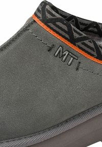 Chaussures en suede grises avec des coutures orange et un col noir à motifs. Présentent un logo embossé "MT" et des semelles en caoutchouc grises lisses.