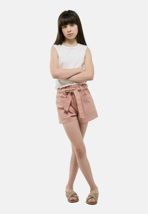 Shorts en coton rose clair avec une taille ceinturée et des poches avant, associés à un haut sans manches blanc et des sandales tressées.