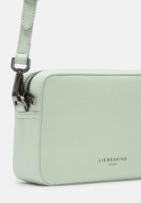 Hellgrüne Ledertasche mit Reißverschluss, rechteckiger Form und verstellbarem Tragegurt. Verfügt über den eingravierten Markennamen auf der Vorderseite und silberne Beschläge.