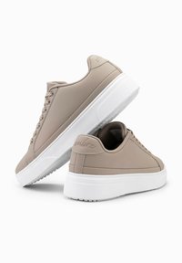 Baskets basses beige en matériau synthétique lisse, avec une semelle en caoutchouc blanc, un bout rond et plusieurs œillets pour les lacets.