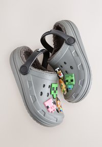 Sabots gris avec une doublure douce et duveteuse, présentant quatre breloques colorées à thème fixées à l'avant et une sangle arrière robuste.