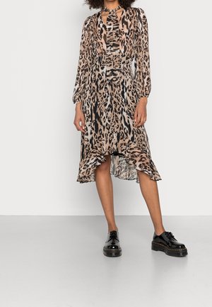 Kvinde iført en langærmet kjole med leopardprint og flæsekant kombineret med sorte skinnende snørestøvler på plateau.