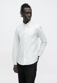 Camisa abotonada en gris claro con finas rayas blancas. Hecha de un tejido suave, cuenta con cuello estándar y mangas largas.