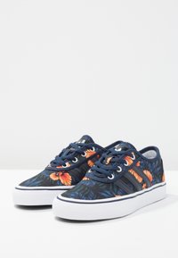 Blå sneakers med blommönster och orangea samt gröna detaljer, med ovandel av tyg, vit gummisula och snördesign.