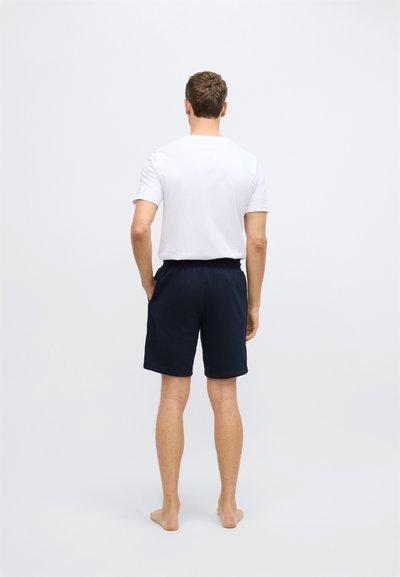 Férfiak hátulnézetből, fehér rövid ujjú pólót és tengerészkék rövidnadrágot viselve, egyszínű mintával és kényelmes szabással. Síma és egyenletes szövettextúra.