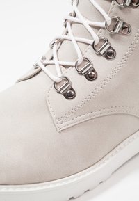 Stivale beige con lacci, occhielli in metallo, materiale a trama liscia e suola in gomma bianca. Presenta cuciture in contrasto.