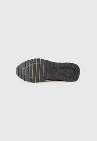 Schuhsohle mit einer strukturierten Gummioberfläche, die tiefe Profilmuster für besseren Halt aufweist. Beinhaltet sichtbare Markenkennzeichnungen und flexible Rillen für mehr Beweglichkeit.