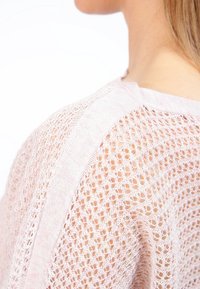 Pull en tricot rose clair avec un motif de dentelle ajouré. Il présente un col rond et de subtiles textures le long des bords.