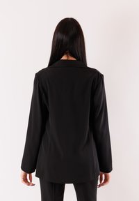 Blazer nero con maniche lunghe, colletto a revers e texture liscia. Vestibilità sagomata con una struttura sottile sul retro.