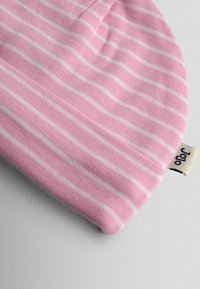 Bonnet pour bébé en maille rayé rose doux et blanc avec un bord replié et une petite étiquette en tissu attachée sur le côté.