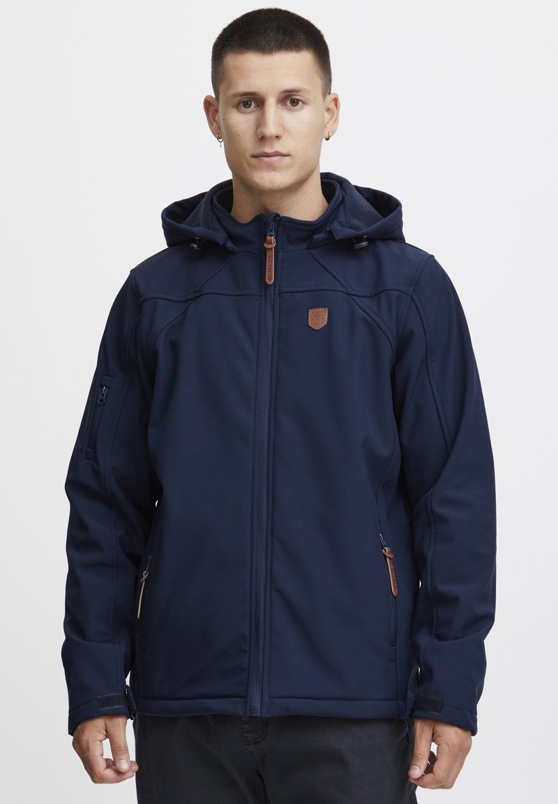 Veste softshell bleu marine avec fermeture éclair à l'avant, capuche ajustable, poches latérales et accents en cuir marron. Textures légère et lisse.