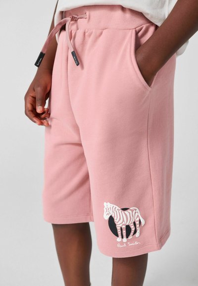 Person iført lyserøde shorts til knæene med forlommer foran og en hvid zebra-grafik på den nederste venstre ben.