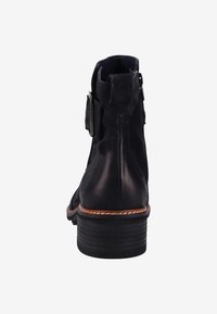 Botín negro de cuero hasta el tobillo con tacón apilado, cremallera lateral y una gran hebilla decorativa en el lado exterior, mostrado desde la vista trasera.