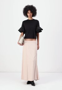 Schwarzes, gekürztes Oberteil mit Puffärmeln, kombiniert mit einem hellrosa Maxikleid mit seitlichen Knöpfen. Accessoires: eine weiße Handtasche und schwarze Stiefel.