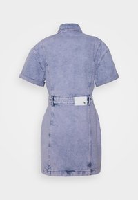 Vaalean violetti farkumekko lyhythihaisilla, käännetyillä hihoilla, kauluksella, vyölenkeillä ja kangasvyöllä, jossa on valkoinen etiketti takana.